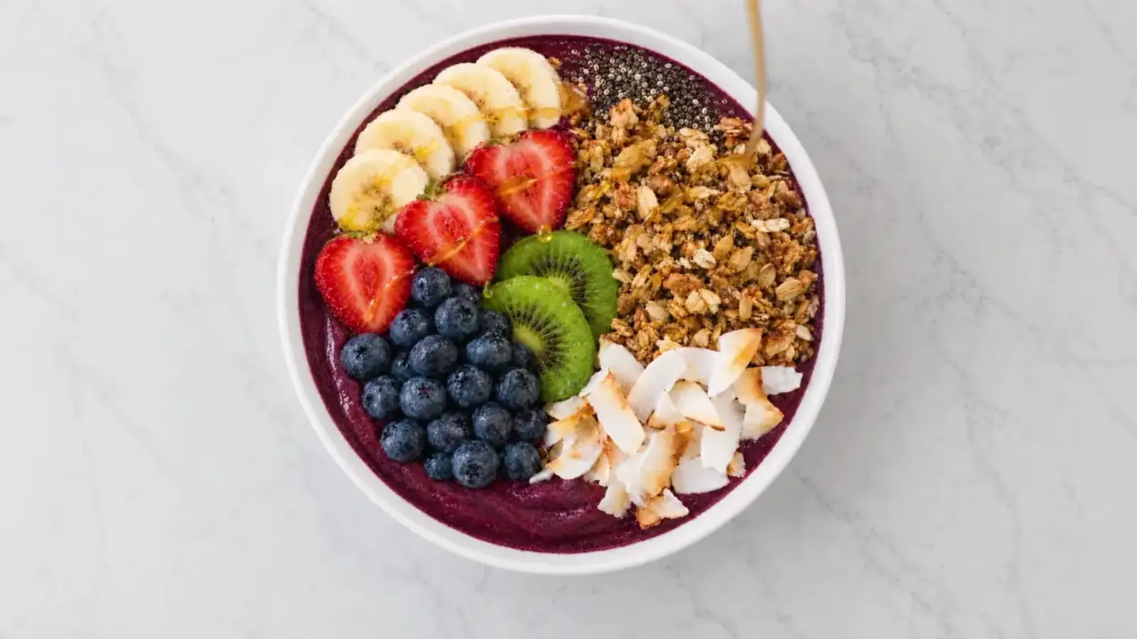 The end of the 208 Acai home page film: honey drizzled over a finished acai bowl with banana, strawberries, kiwi, blueberries, granola and coconut